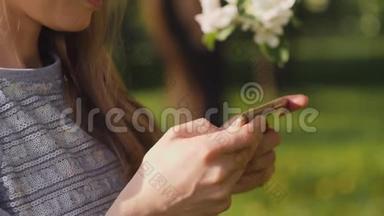 在<strong>春城</strong>散步的苹果树盛开的枝条背景下，漂亮的女人用智能手机短信